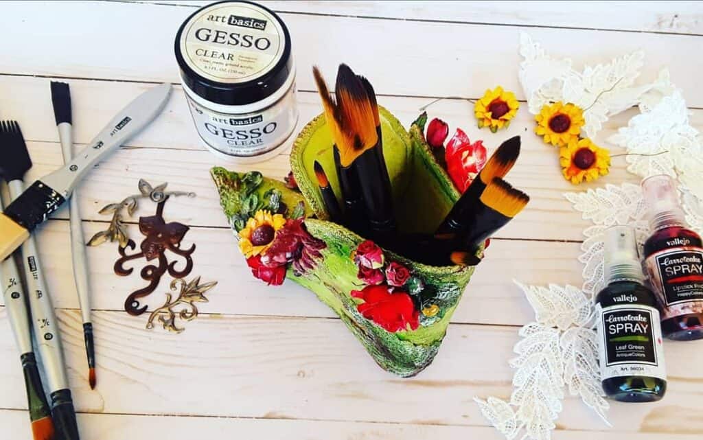 Pinceles, gesso y accesorios de arte en mesa de madera para manualidades creativas.